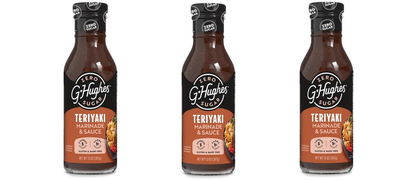 Three bottles of G Hughes Teriyaki Marinade and Sauce are displayed, featuring a dark brown liquid in clear glass containers with labels highlighting "Zero Sugar," "Gluten & Dairy Free," and nutritional information.