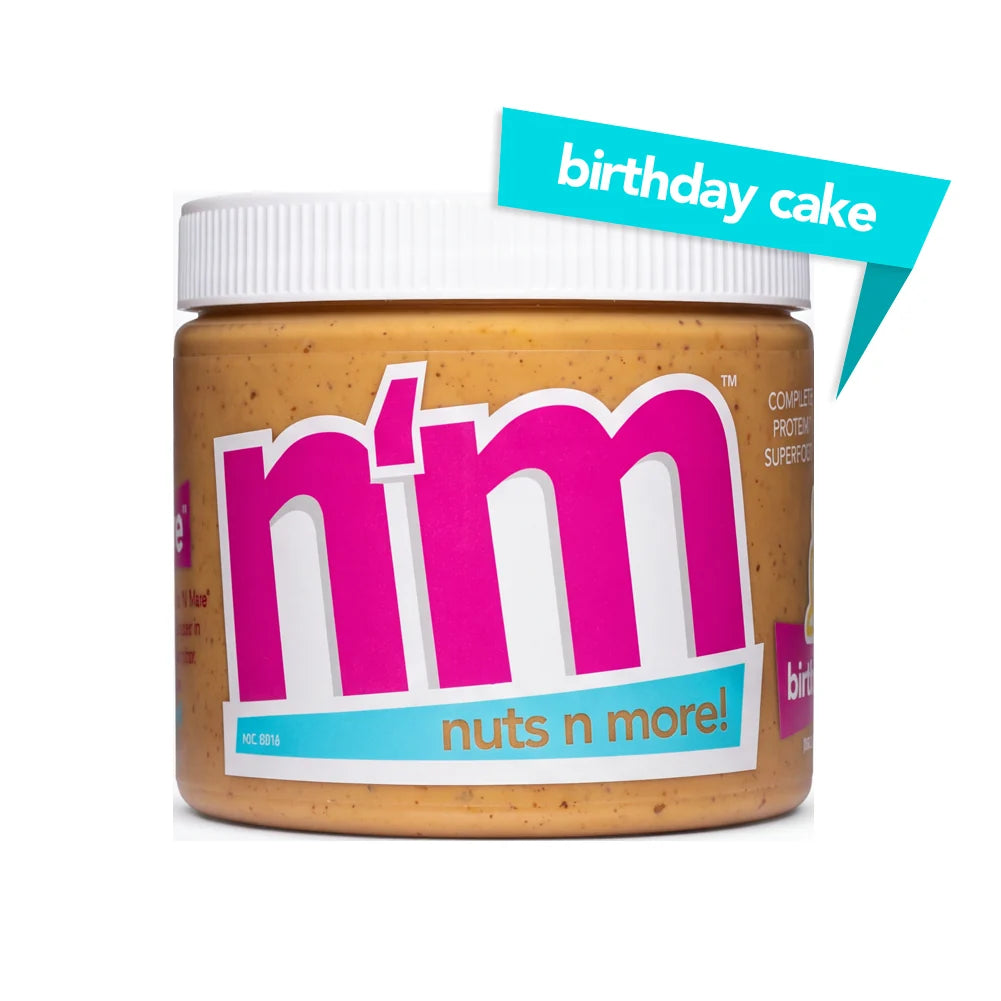A jar of "n'm" peanut butter with a birthday cake flavor label prominently displayed, featuring bright pink and blue text against a light brown background.