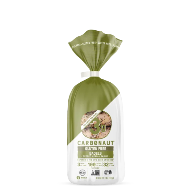 A green and white bag of Carbonaut gluten-free bagels, labeled "Seeded Herb & Garlic," displays nutritional information, including "3g protein" and "100 calories," with a twist tie at the top.