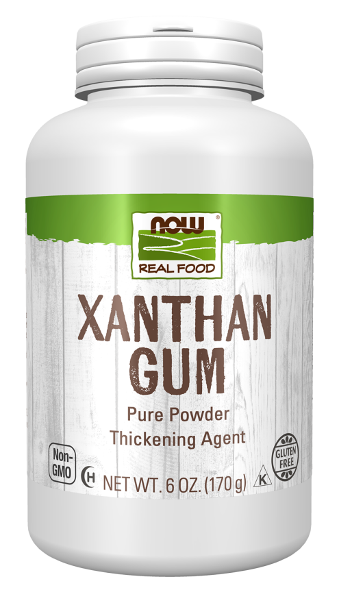 A white bottle of NOW Real Food Xanthan Gum, labeled as a pure powder thickening agent, with a wooden background, indicating it is gluten-free and non-GMO.