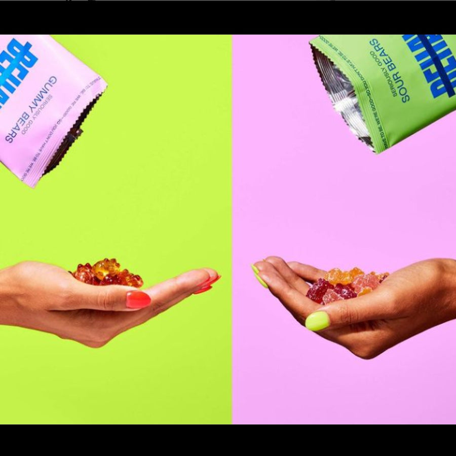 Two hands, one with pink nails and the other with green nails, hold colorful gummy bears, with a bright green background on the left and a pink background on the right, showcasing Seriously Good Sweet and Sour Gummy Bears.