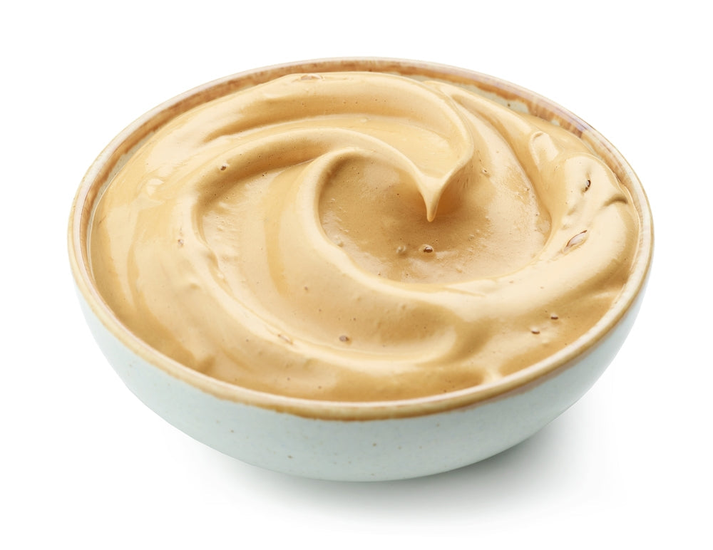 A creamy mocha pudding is swirled in a light-colored bowl, showcasing its smooth, rich texture and inviting golden-brown hue against a white background.