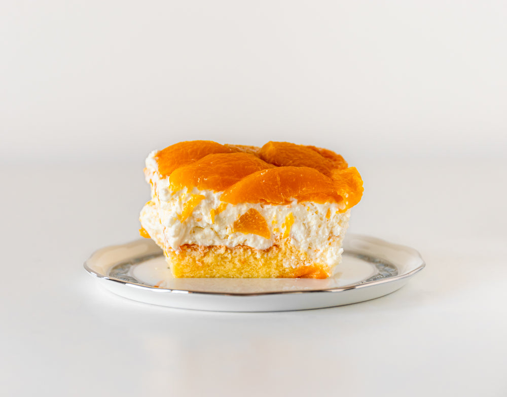 A slice of fluffy peach dessert topped with bright orange peach slices sits on a silver plate against a plain white background.