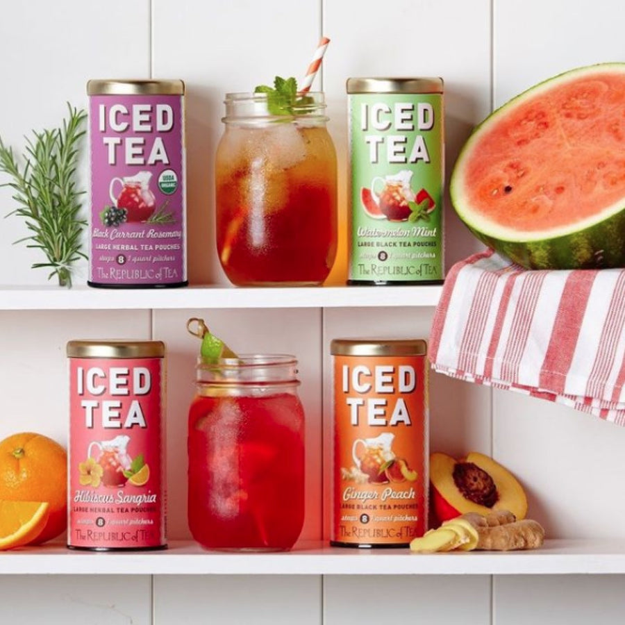 Four colorful cans of iced tea from The Republic of Tea are displayed on a shelf, alongside a mason jar filled with iced tea and garnished with mint, with fresh fruit like watermelon, orange, and peach nearby.