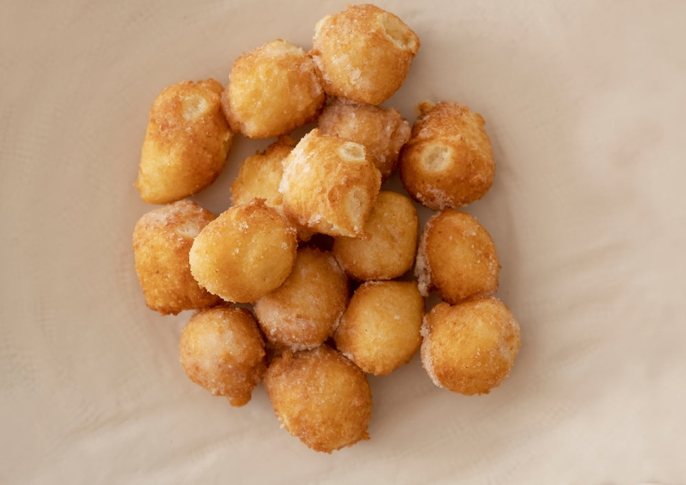 A pile of golden-brown, bite-sized lemon puffs is arranged neatly on a light-colored plate, showcasing their crispy texture and sugary coating.
