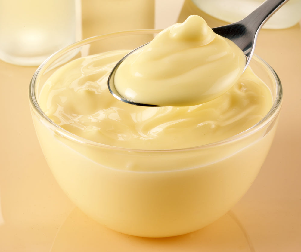 A spoon lifts a creamy, yellow mock rice pudding from a clear glass bowl, set against a soft, light-colored background.