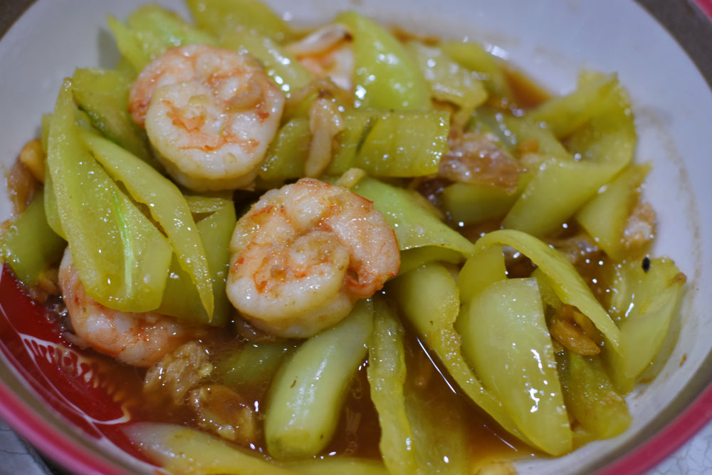 A bowl filled with cooked shrimp and green vegetables, featuring a glossy sauce, showcases a colorful and appetizing dish, likely related to a seafood recipe.