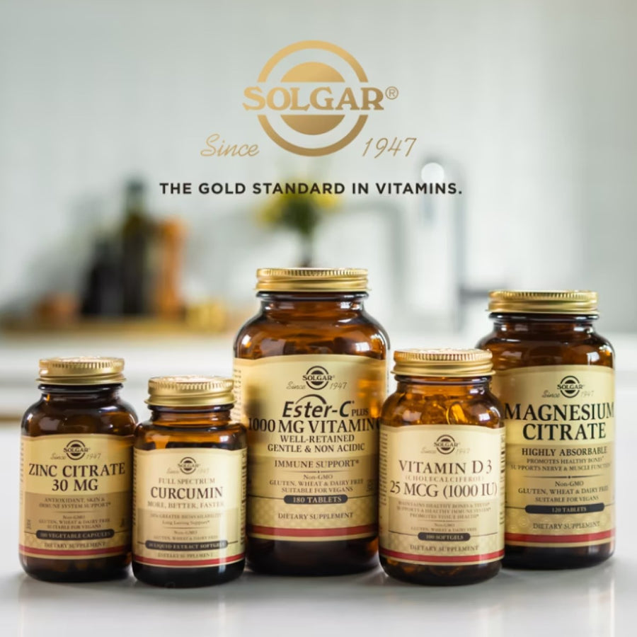 Five amber glass bottles of Solgar dietary supplements, including Ester-C, Vitamin D3, and Magnesium Citrate, are displayed on a kitchen countertop with a blurred background.