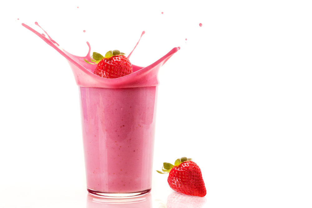 A glass filled with a pink smoothie splashes as a fresh strawberry sits beside it, highlighting a refreshing and vibrant drink.