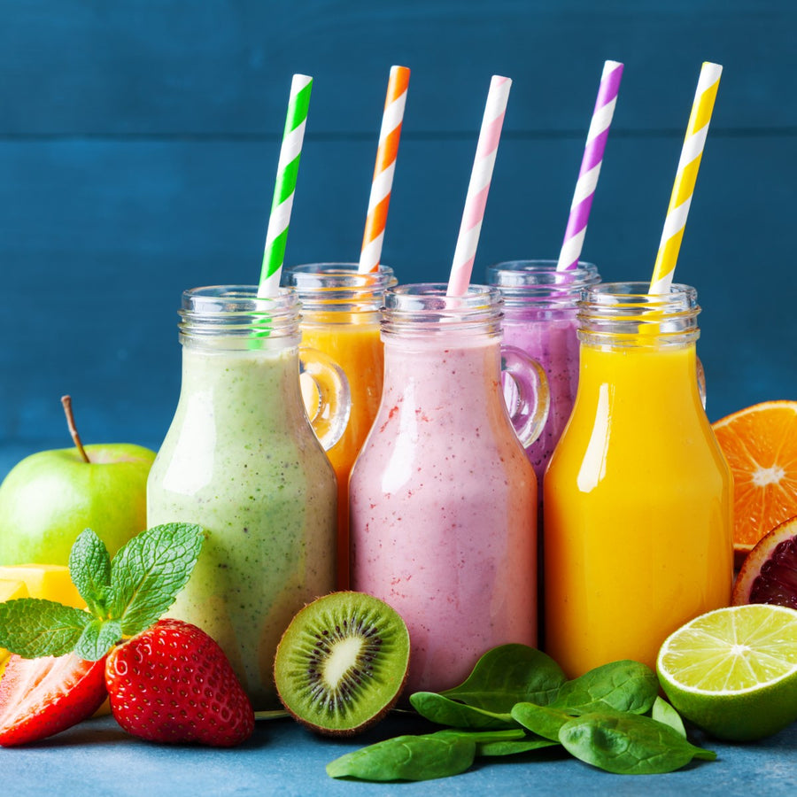 Six colorful smoothie bottles with striped straws are arranged on a blue background, surrounded by fresh fruits like strawberries, kiwi, and an apple, highlighting bariatric-friendly drink options.