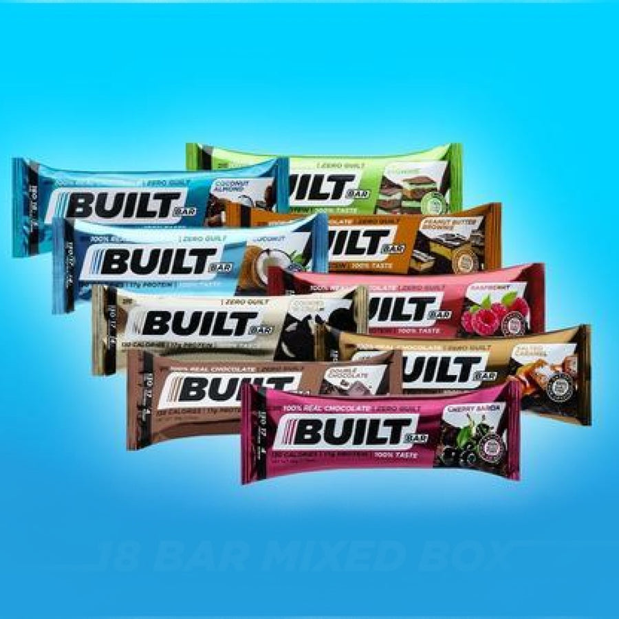 A variety of BuiltBar protein bars in different flavors are displayed against a bright blue background, showcasing their colorful packaging and branding.