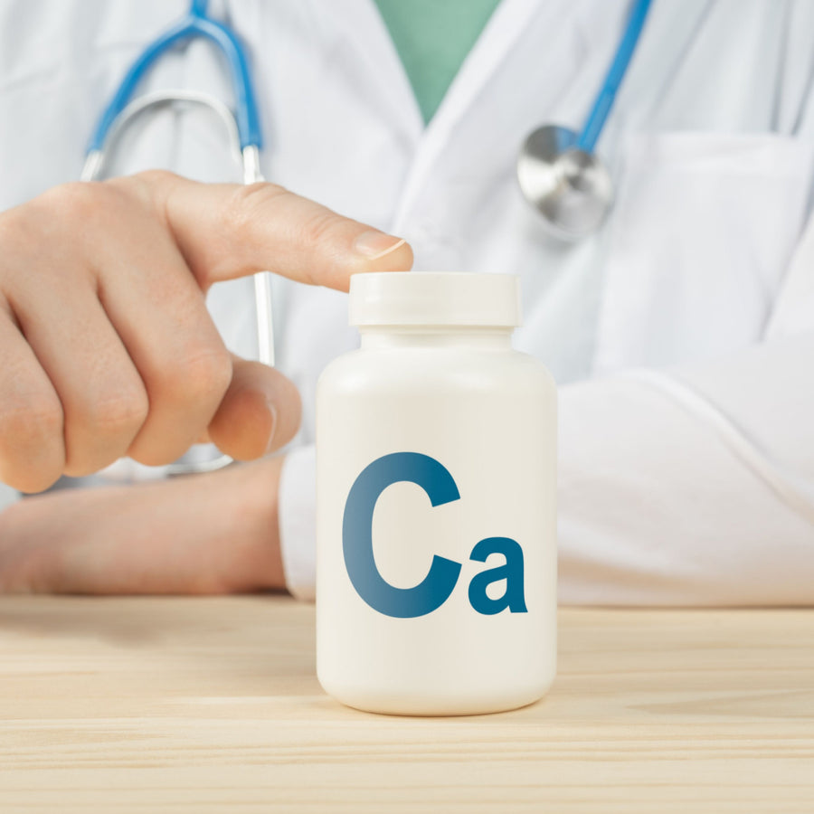 A healthcare professional's hand points to a white bottle labeled "Ca" for calcium, emphasizing its importance after bariatric surgery, with a stethoscope visible in the background.