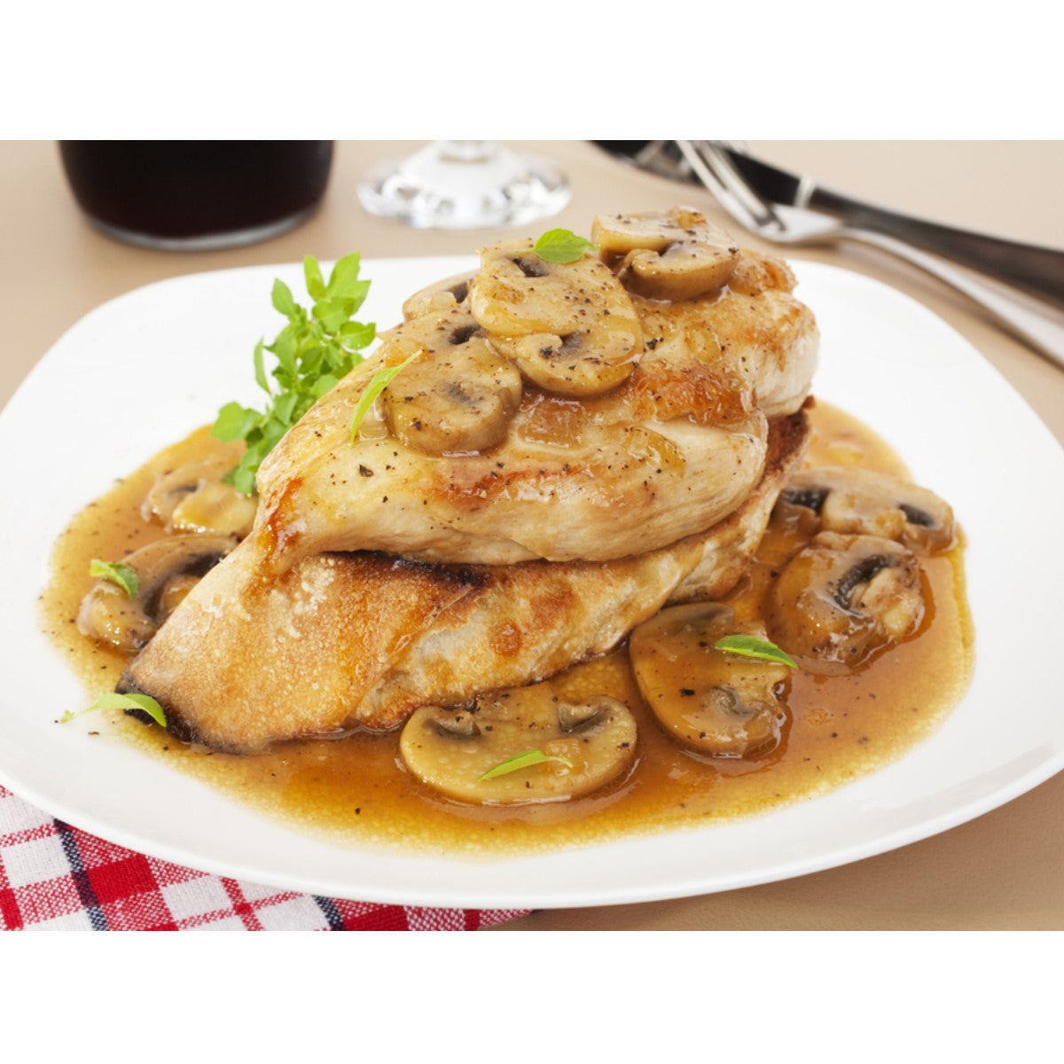 A plate of chicken piccata features two chicken breasts topped with sliced mushrooms and a savory sauce, garnished with fresh herbs, set against a neutral table background.