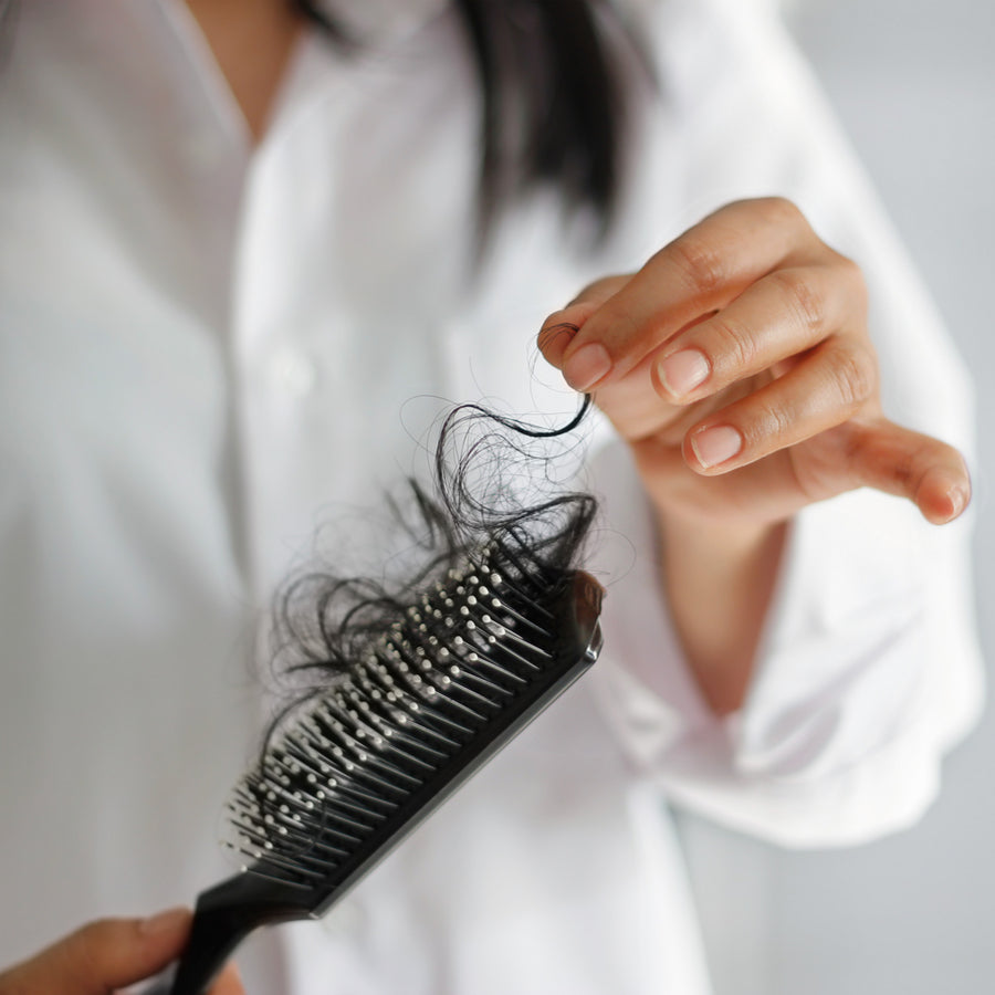 A person in a white shirt holds a hairbrush with loose hair strands while examining a single hair, illustrating concerns about hair loss after bariatric surgery.