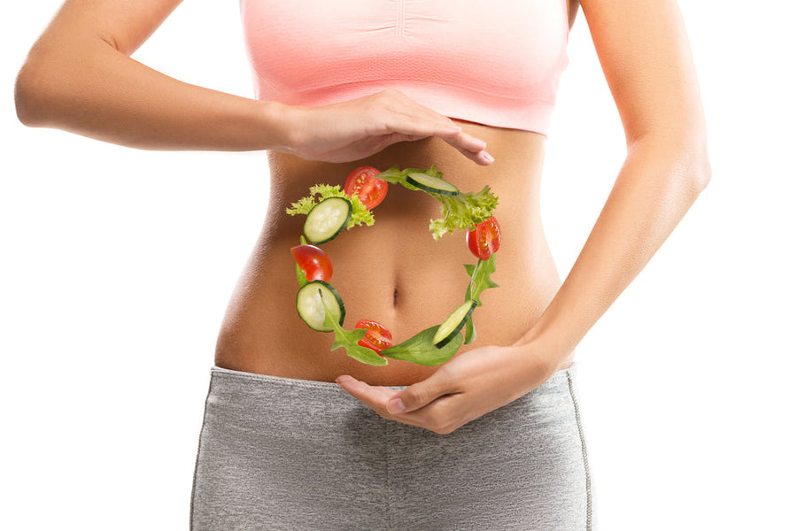 A person in a pink crop top and gray leggings holds their hands around their waist, forming a circle with fresh vegetables like tomatoes and cucumbers, symbolizing healthy eating and weight management.