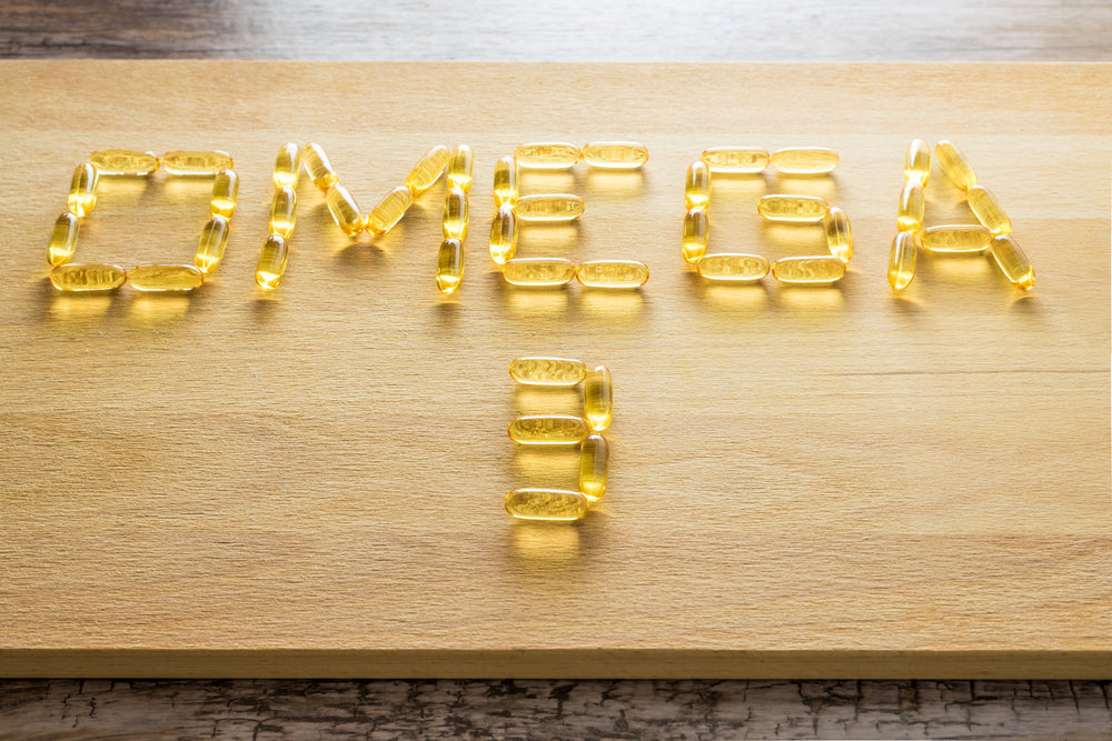 Yellow gel capsules are arranged on a wooden surface to spell out "OMEGA 3," highlighting the focus on omega-3 supplements in relation to health and nutrition.