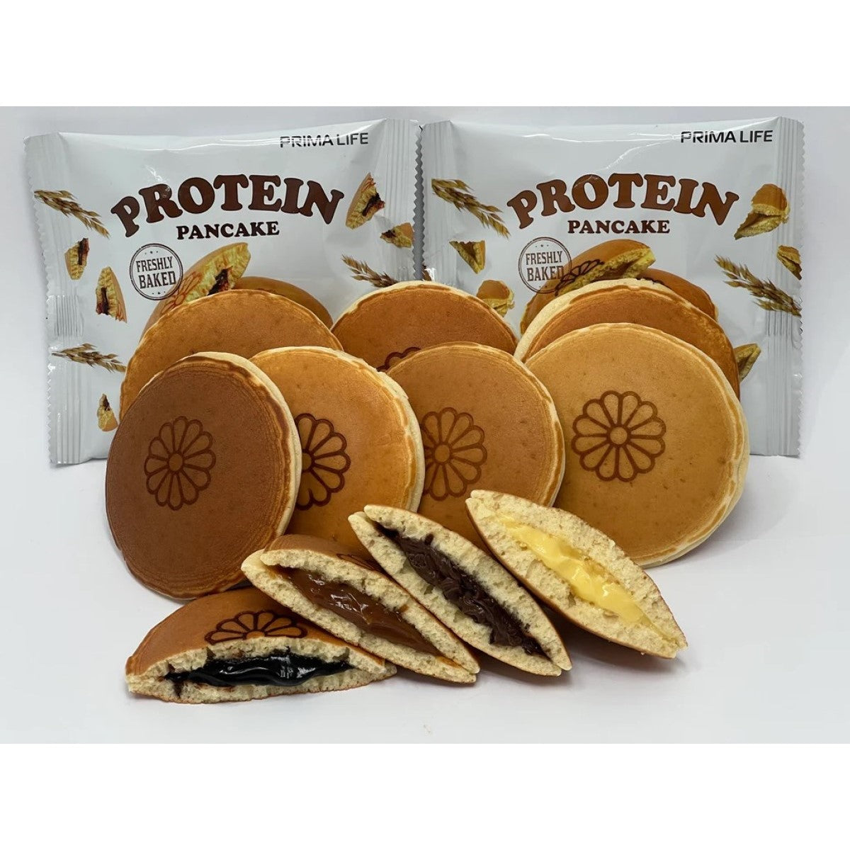 A variety of Prima Life protein pancakes are displayed, featuring whole pancakes with a flower design, some cut in half to reveal fillings of chocolate and cream, alongside packaging in the background.