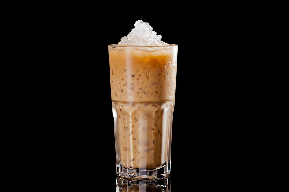 A tall glass filled with iced cappuccino, featuring a creamy brown mixture topped with crushed ice, is set against a black background.