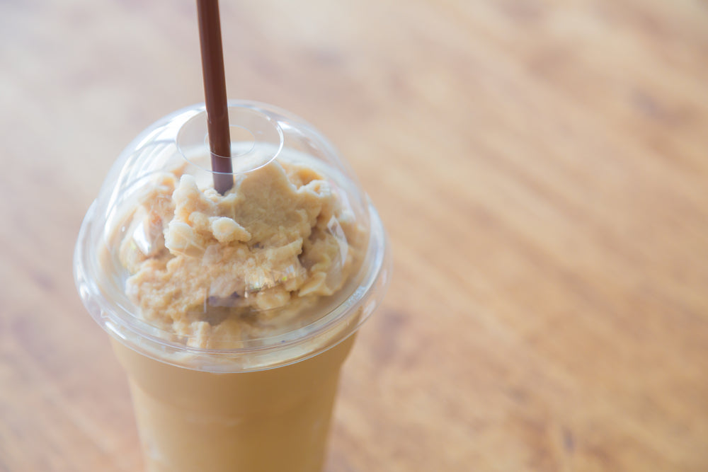 A caramel latte topped with whipped cream and a brown straw sits on a wooden table, showcasing its creamy texture and inviting appearance.