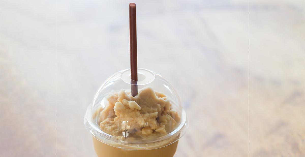 A clear cup filled with spiced iced coffee topped with creamy foam and a brown straw sits on a wooden surface, inviting a refreshing drink experience.