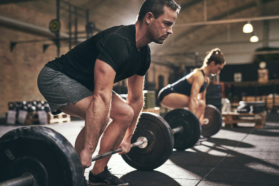 A man and a woman, both focused and determined, are performing deadlifts with heavy weights in a gym setting, emphasizing strength training after bariatric surgery.