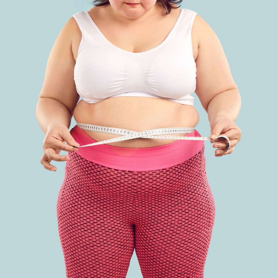 A person in a white tank top and pink leggings measures their waist with a tape measure, focusing intently, against a light blue background, highlighting the importance of tracking health beyond weight.