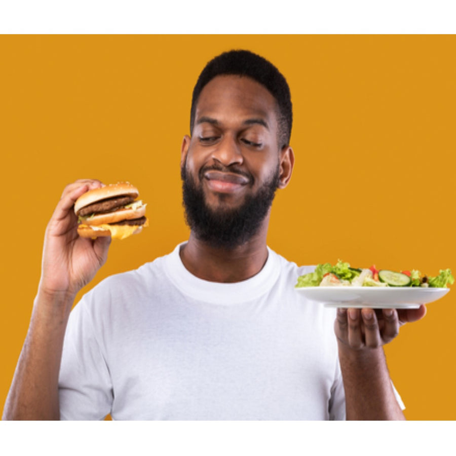 A man with a beard smiles while holding a hamburger in one hand and a plate of salad in the other, set against a bright orange background, illustrating food swap choices for better nutrition.