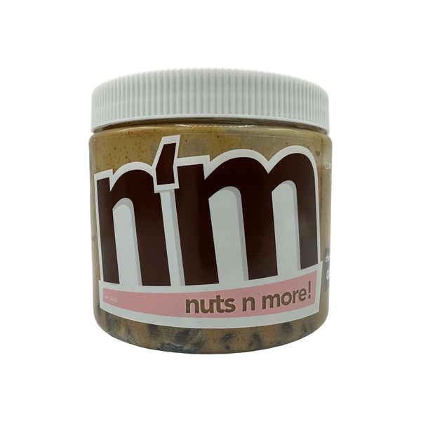 A clear jar of nut butter labeled "n'm" with a white lid, featuring a bold brown logo and the tagline "nuts n more!" on a pink band, set against a black background.