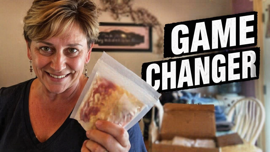 A smiling woman holds a clear bag with food inside, standing in a kitchen with boxes in the background, promoting a product labeled "Game Changer."