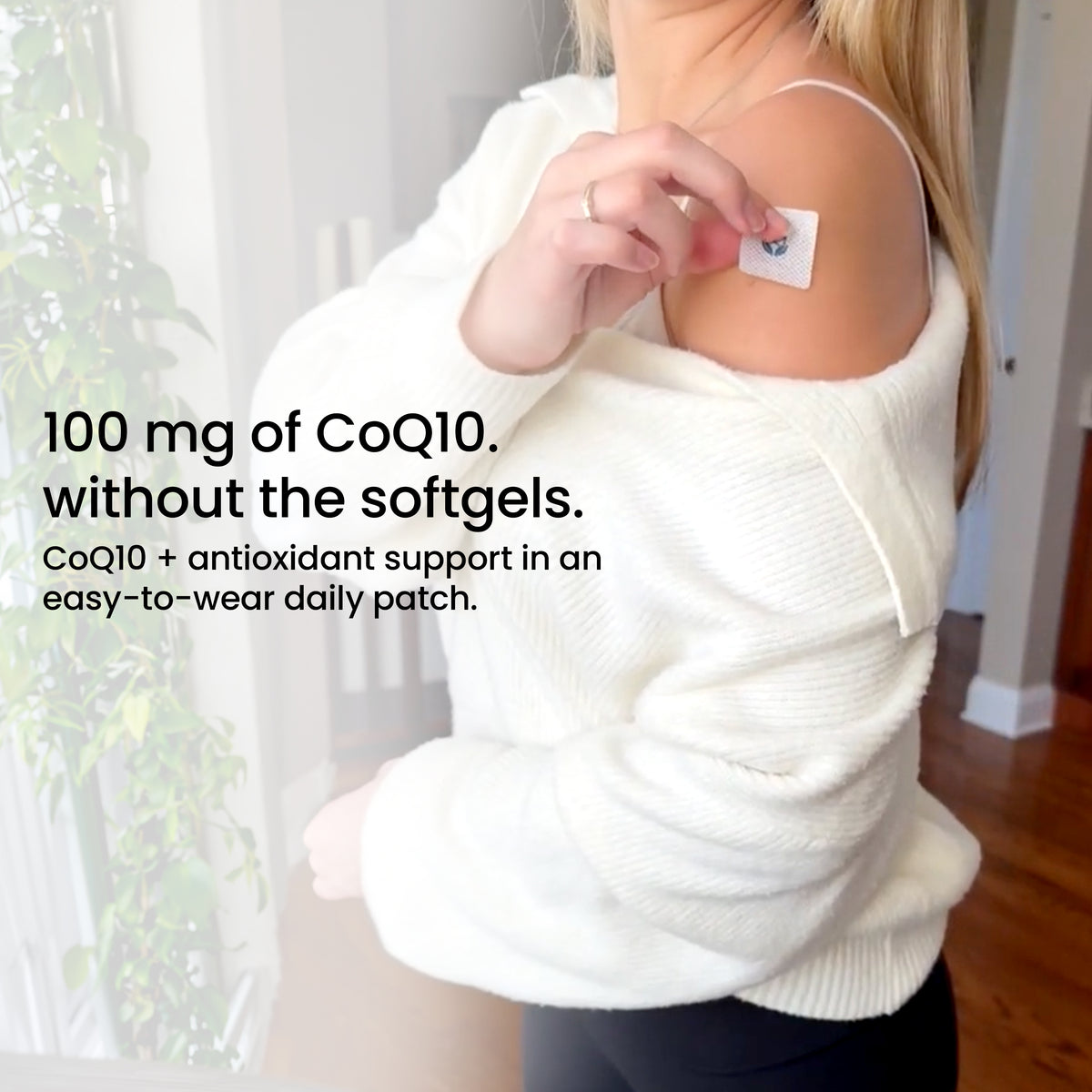 A woman in a white sweater applies a CoQ10 patch to her shoulder, promoting antioxidant support without the need for softgels, in a bright indoor setting.