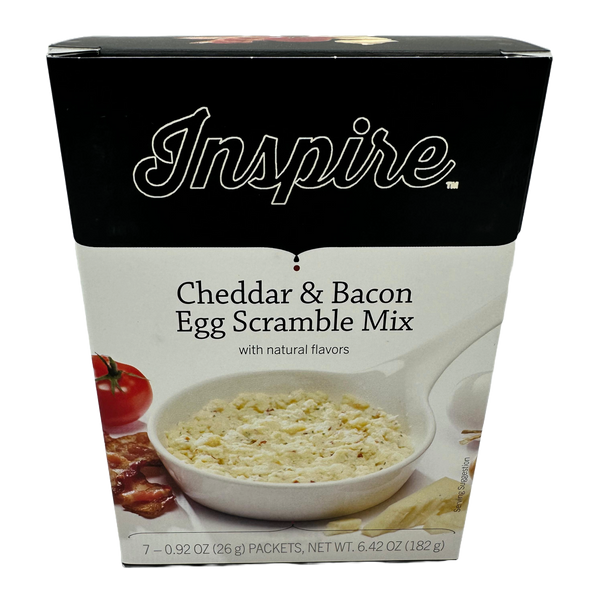 A box of Inspire Cheddar & Bacon Egg Scramble Mix features a bowl of the mix with a creamy texture, alongside a tomato and bacon, highlighting its natural flavors and serving suggestion.