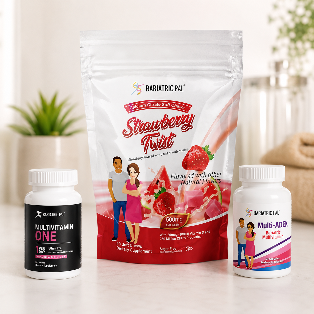 Three Bariatric Pal supplement products arranged on a light countertop: a large Strawberry Twist pouch in the center, with two white bottles at the sides labeled Multivitamin One and Multi-Adek. The scene is brightly lit with a soft blurred indoor background and small plants.