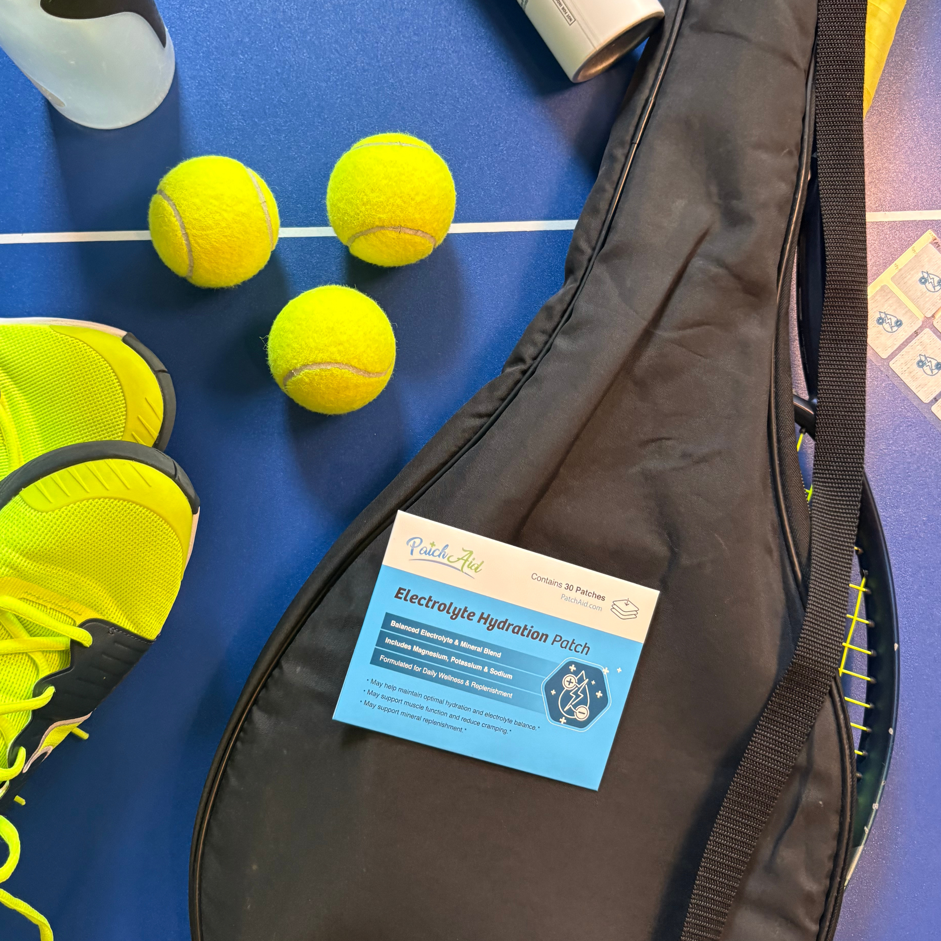 Tennis balls, shoes, and a bag on a blue surface with electrolyte hydration patches. 