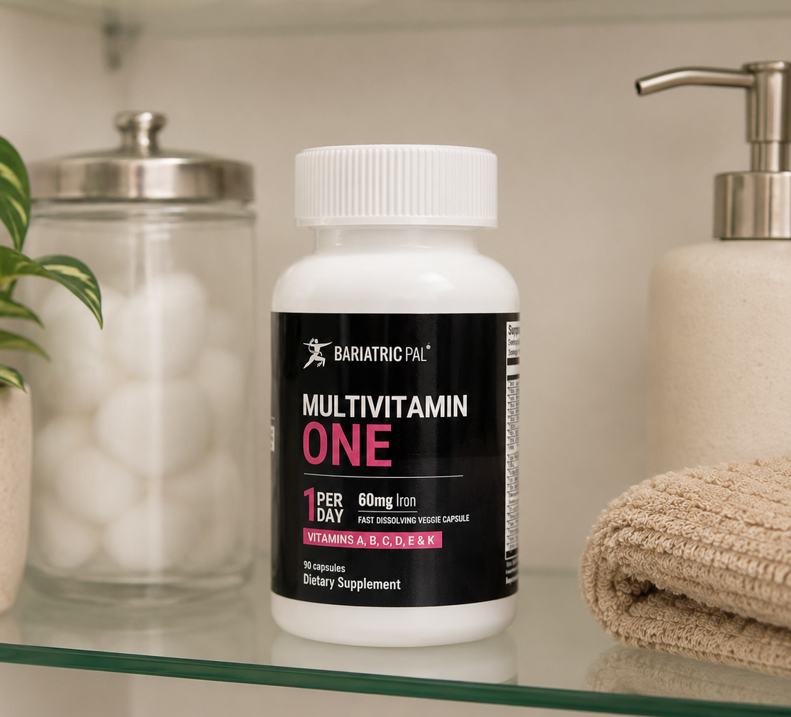 A white bottle of Bariatric Pal Multivitamin One, labeled with "1 Per Day" and "60mg Iron," is displayed on a shelf next to a plant and a beige towel in a bathroom setting.
