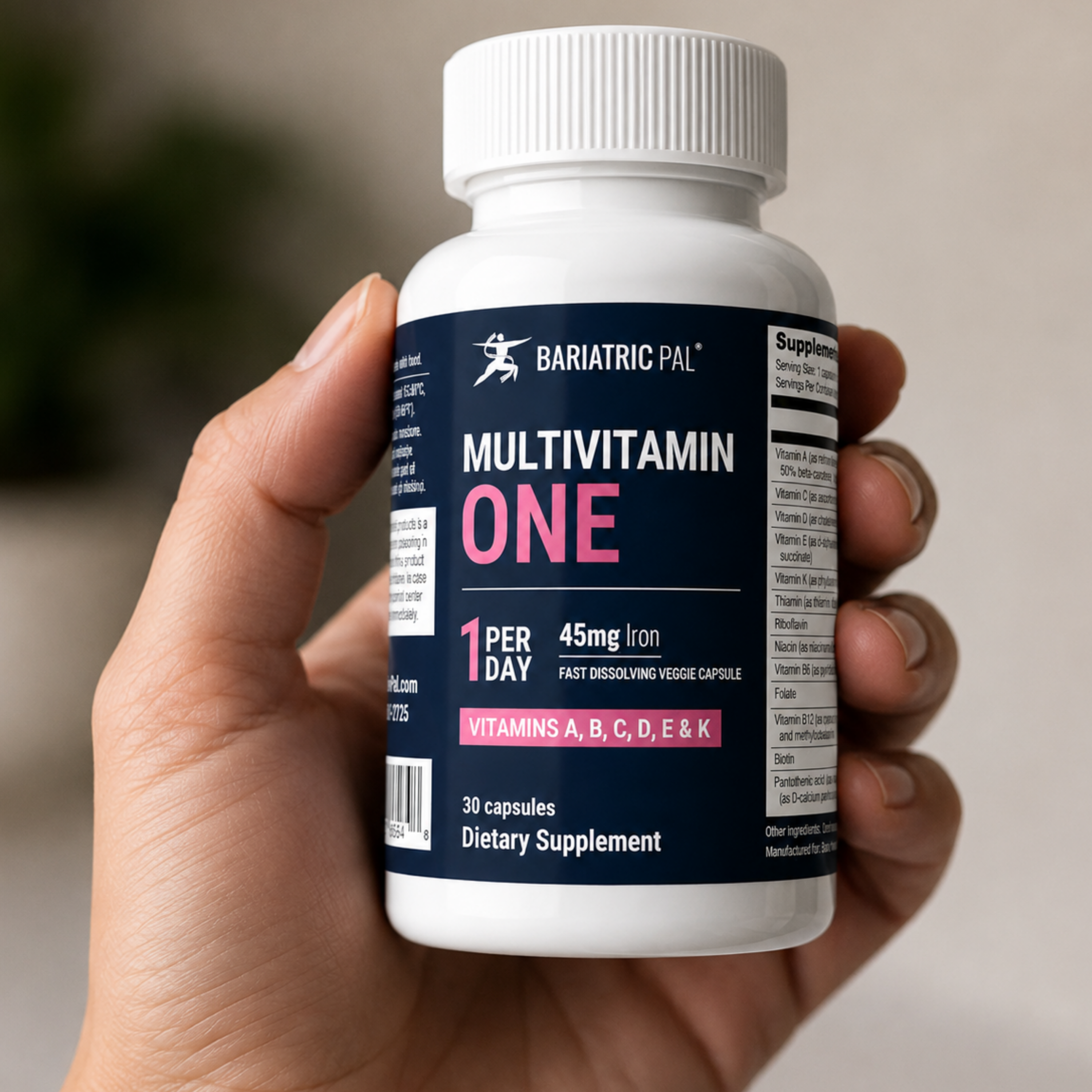 A hand holding a white bottle of BariatricPal Multivitamin One supplement, showing the front label with navy blue, white, and pink text.