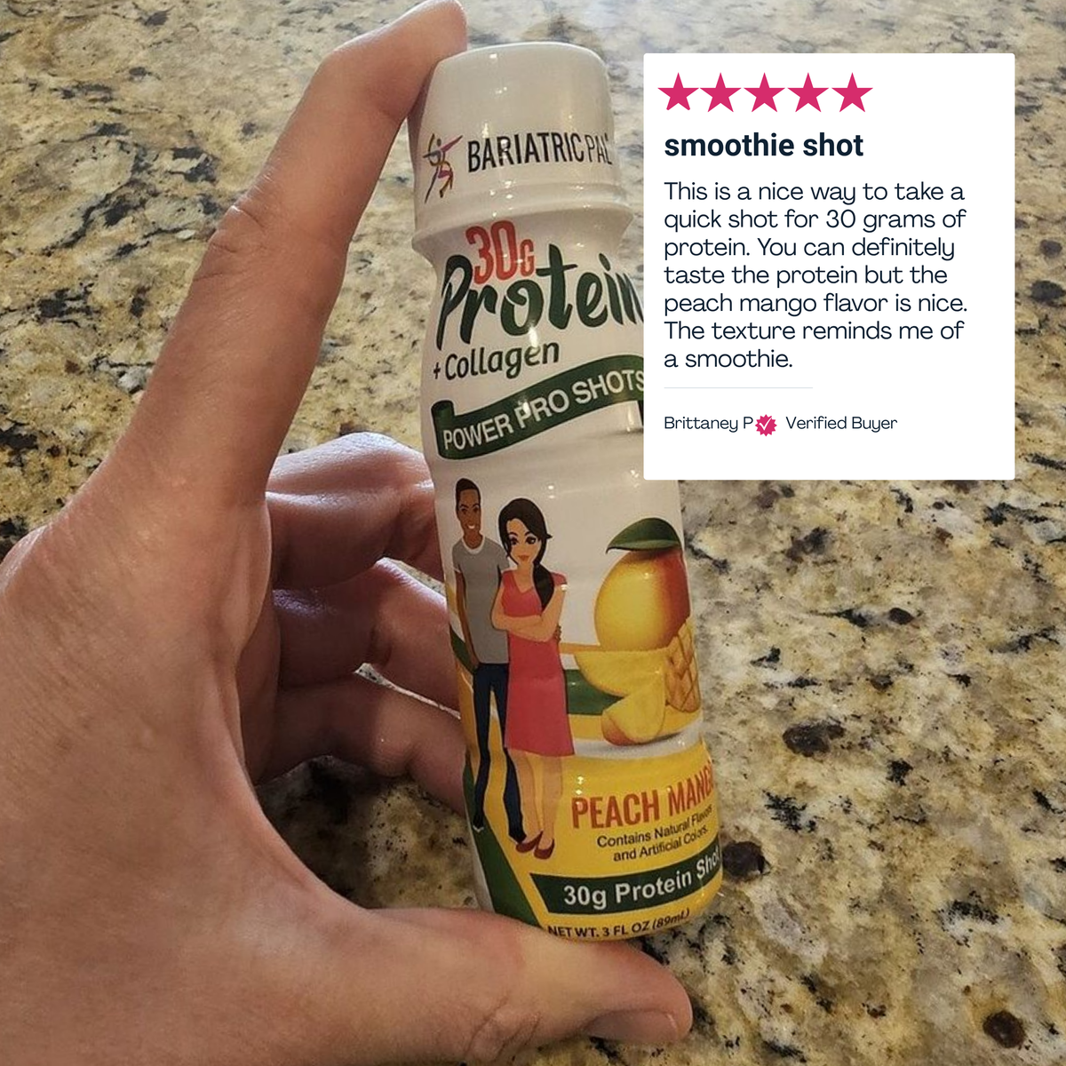 A hand holds a bottle of peach mango protein shot on a granite countertop, featuring illustrations of two people and a label highlighting its 30 grams of protein and collagen content.