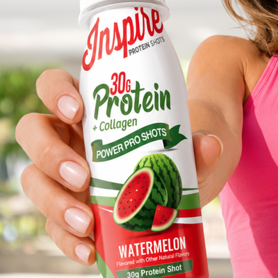 A person in a pink top holds a bottle of Inspire Protein Shots featuring a watermelon design, highlighting 30 grams of protein and collagen in a bright, outdoor setting.