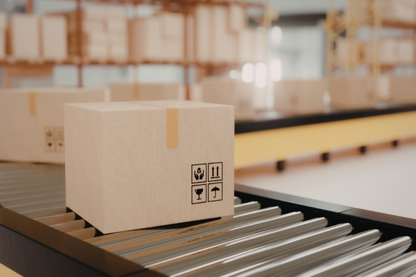Cardboard box with shipping labels on a conveyor belt in a warehouse.