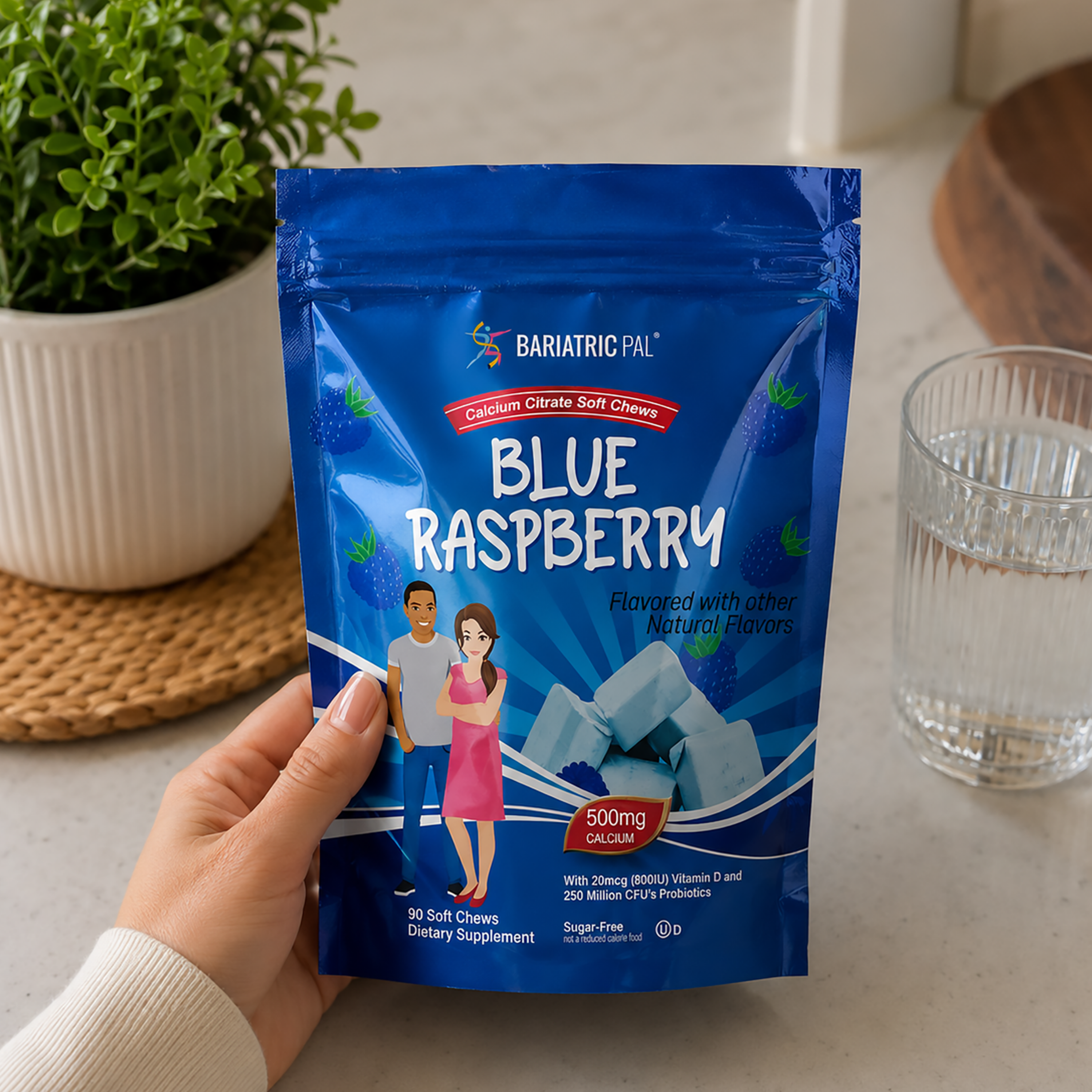 A hand holds a blue stand-up pouch of BariatricPal Blue Raspberry soft chew dietary supplement. The package is blue with white text and illustrations of a couple and blue raspberry pieces.