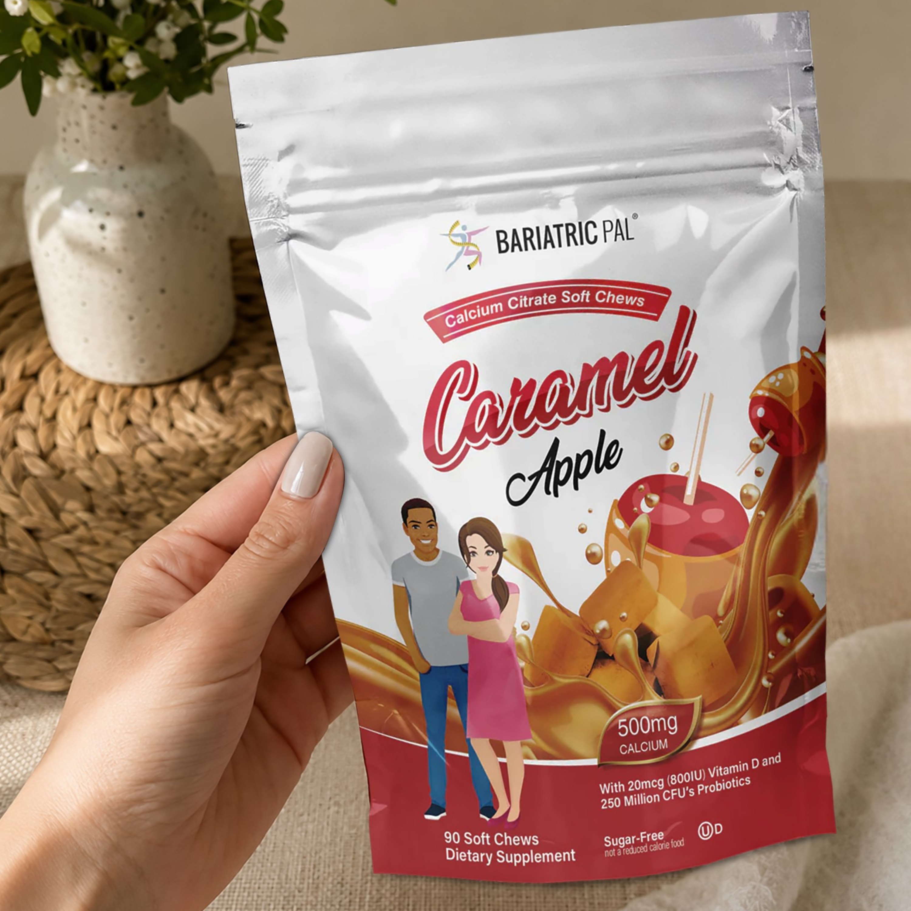 A hand holds a stand-up pouch of BariatricPal Caramel Apple soft chew dietary supplement. The white and red pouch features illustrations of caramel, an apple, and a couple, with text indicating 90 soft chews and 500mg calcium.