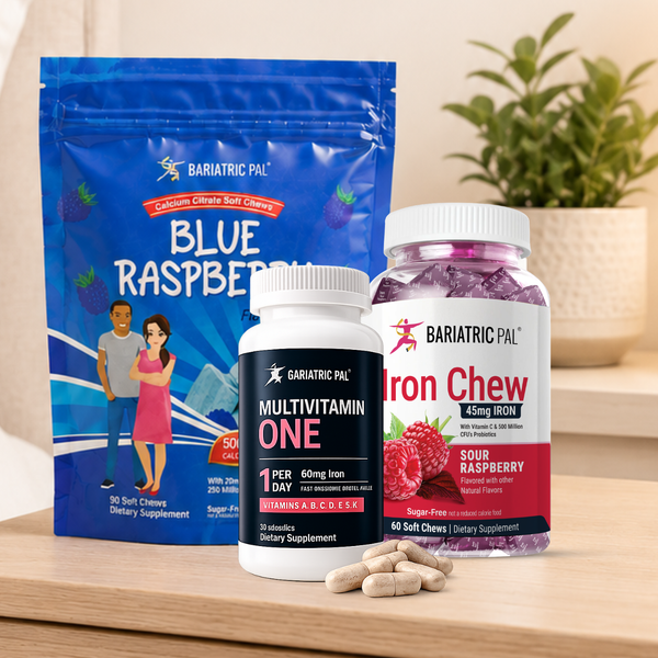 Three Bariatric Pal dietary supplement products arranged on a wooden surface: a large blue Raspberry Soft Chew pouch, a white bottle of Multivitamin One softgels, and a white bottle of Sour Raspberry Iron Chew tablets, with a few beige softgels in front. A potted plant is blurred in the background.