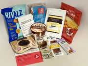 A variety of protein-rich snacks and meal options are displayed, including a packet of cheese-flavored snacks, pudding mix, protein bars, and chips, all arranged on a neutral background.