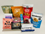 A variety of snack products is displayed on a white surface, including noodles, chips, gummies, protein bars, and cookies, showcasing colorful packaging and diverse flavors.