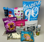 A variety of protein snacks and supplements are displayed, including protein pretzels, gummy bears, and flavored powders, all arranged on a light background for an e-commerce product showcase.