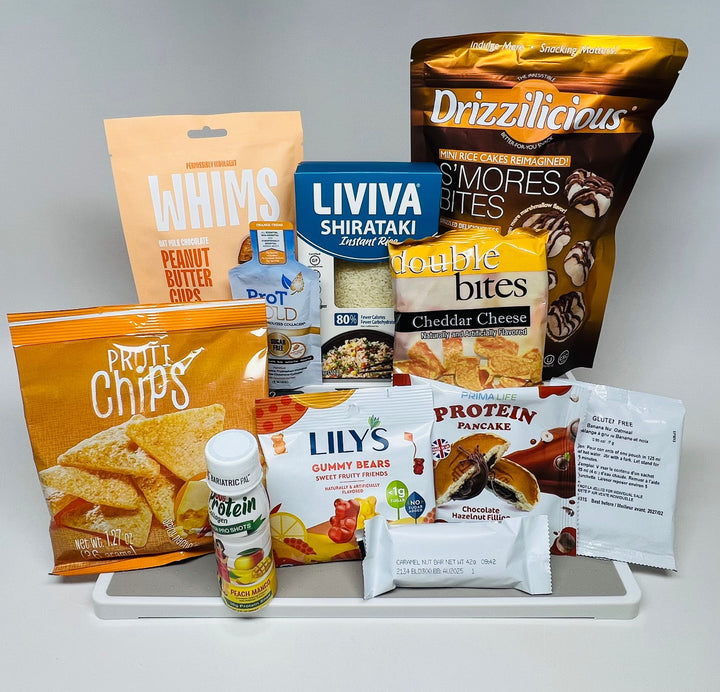 A variety of snack products is displayed on a white surface, including peanut butter cups, shirataki rice, cheddar cheese bites, gummy bears, and protein drinks, all arranged for an appealing presentation.