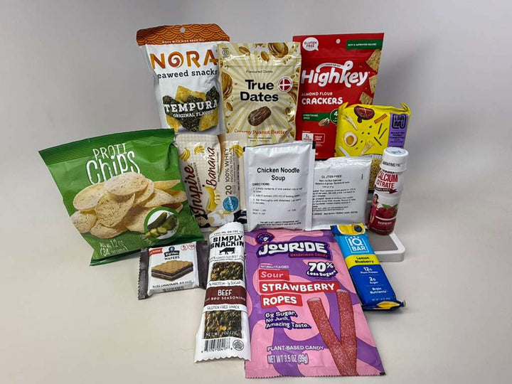 A variety of packaged snacks and food items, including seaweed snacks, crackers, soup, and candy, are arranged on a white surface, showcasing options for healthy eating and snacking.