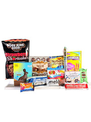 A variety of snacks and treats, including pork rinds, chocolate bunnies, and candy, are arranged on a white surface, showcasing colorful packaging and diverse flavors.