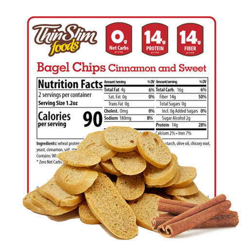 Cinnamon-flavored bagel chips are piled in front of a nutrition facts label, highlighting 0 net carbs, 14 grams of protein, and 14 grams of fiber per serving, with cinnamon sticks beside the chips.