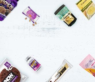 Various snack products, including cookies, protein bars, and supplements, are arranged on a white background, showcasing their colorful packaging and labels.