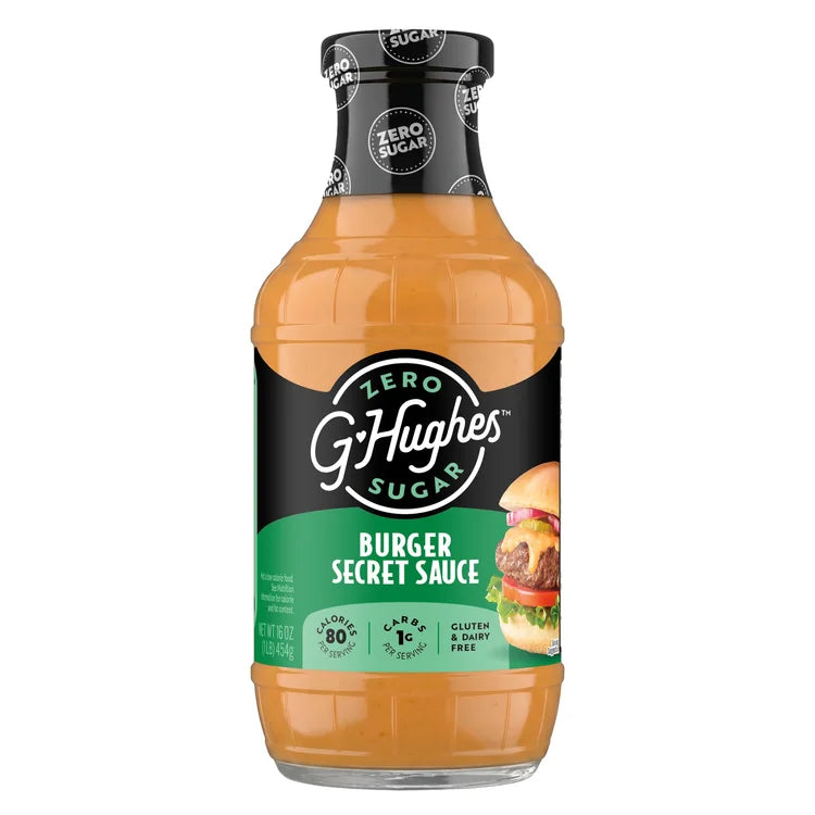 A clear bottle of G. Hughes Burger Secret Sauce, featuring a black and green label with "Zero Sugar" and nutritional information, stands against a plain background, showcasing its rich orange color.